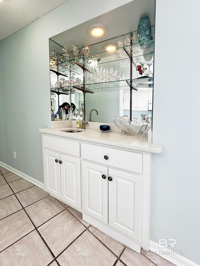 bar featuring white cabinets, light tile patterned floors, a textured ceiling, and sink