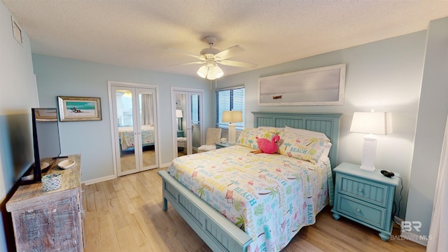 bedroom with two closets, ceiling fan, light hardwood / wood-style floors, and a textured ceiling