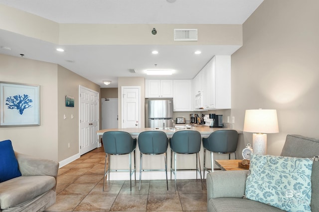 kitchen with freestanding refrigerator, a peninsula, white microwave, recessed lighting, and white cabinets