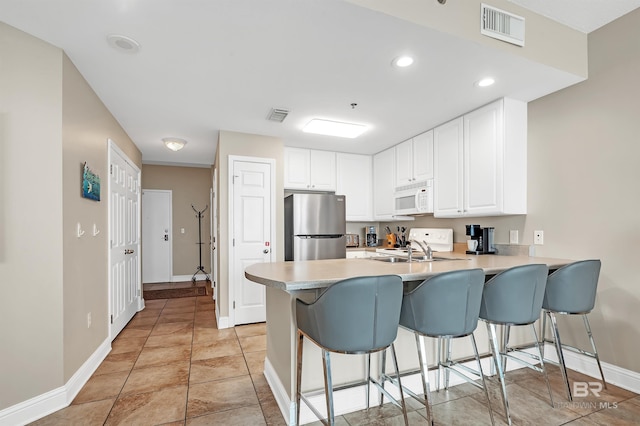 kitchen with white appliances, a peninsula, baseboards, a kitchen breakfast bar, and white cabinets