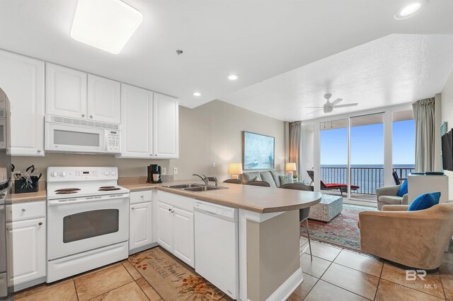 kitchen with white appliances, open floor plan, a sink, a peninsula, and light tile patterned floors