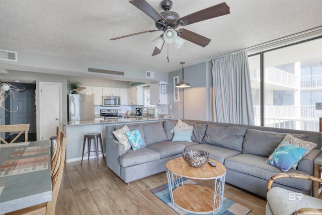 living area featuring ceiling fan, a textured ceiling, light wood-type flooring, and visible vents