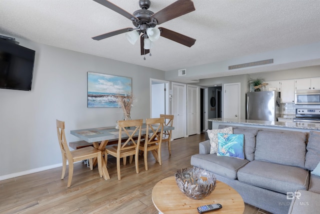 living room featuring light wood-type flooring, baseboards, visible vents, and a textured ceiling