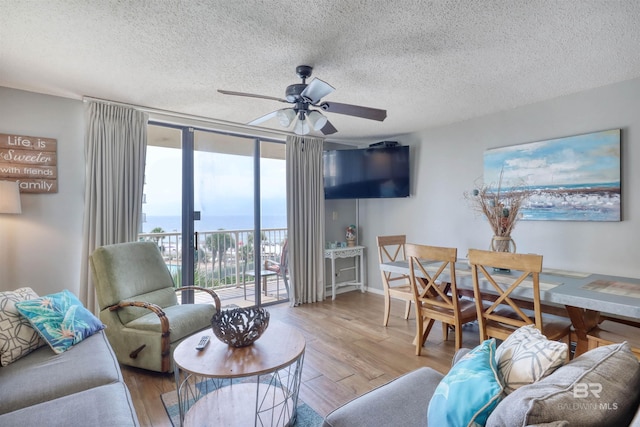 living room featuring ceiling fan, a textured ceiling, floor to ceiling windows, and wood finished floors