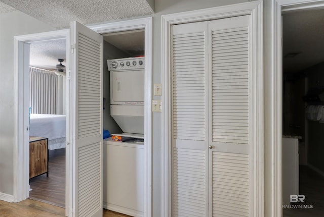 laundry room featuring laundry area, a textured ceiling, stacked washing maching and dryer, and wood finished floors