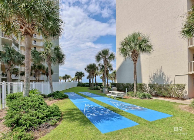 view of community with fence, a lawn, and shuffleboard