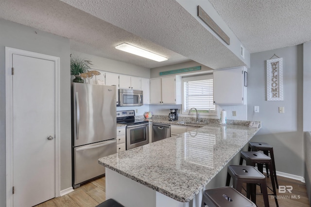 kitchen featuring appliances with stainless steel finishes, a sink, light wood-type flooring, a peninsula, and a kitchen breakfast bar