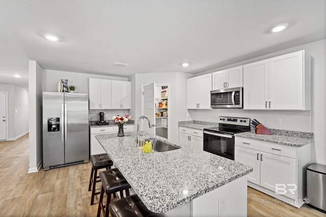 kitchen with a breakfast bar, stainless steel appliances, light wood-style floors, white cabinetry, and a sink