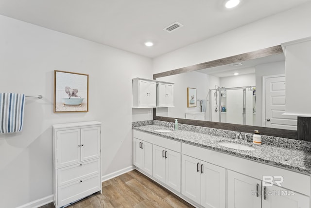 bathroom with wood finished floors, a sink, visible vents, a shower stall, and double vanity