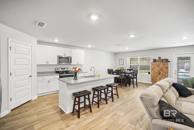 kitchen featuring stainless steel appliances, a sink, light wood-style floors, open floor plan, and a kitchen breakfast bar