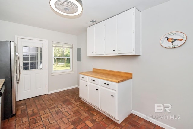 kitchen featuring white cabinetry, brick floor, baseboards, and freestanding refrigerator