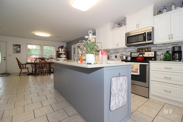 kitchen with appliances with stainless steel finishes, white cabinetry, a center island with sink, and light tile patterned floors