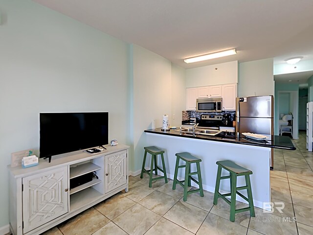 kitchen featuring a kitchen bar, appliances with stainless steel finishes, a peninsula, dark countertops, and decorative backsplash
