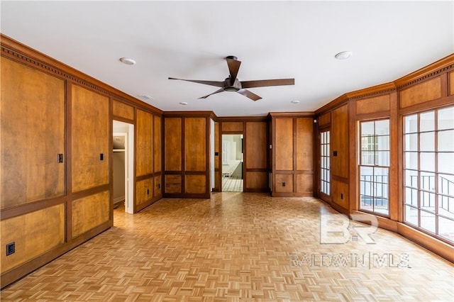 unfurnished room with ceiling fan, crown molding, wooden walls, and light parquet flooring