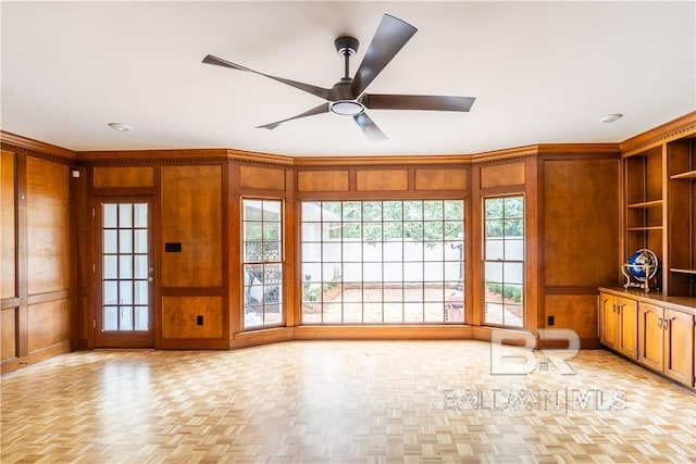 unfurnished living room with built in shelves, wood walls, light parquet floors, and ceiling fan