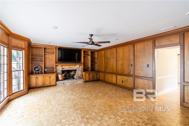 unfurnished living room with ceiling fan, wooden walls, built in features, a fireplace, and light parquet flooring