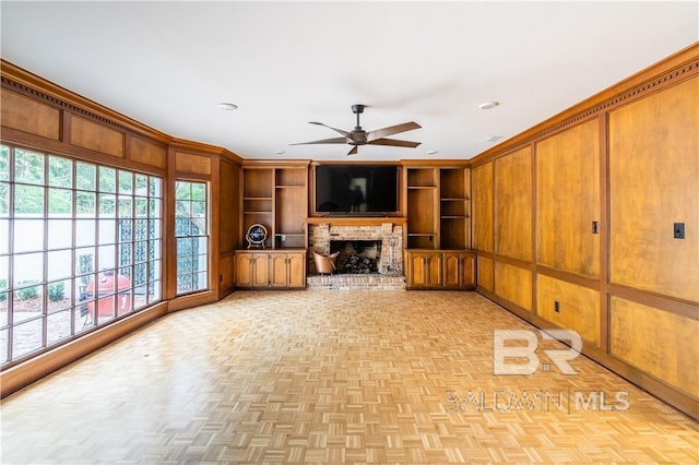 unfurnished living room featuring built in shelves, wood walls, ceiling fan, and light parquet flooring