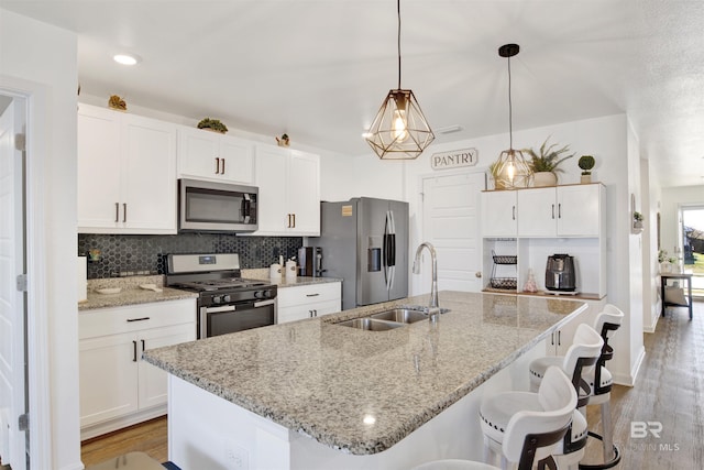 kitchen with appliances with stainless steel finishes, a kitchen island with sink, sink, pendant lighting, and white cabinets