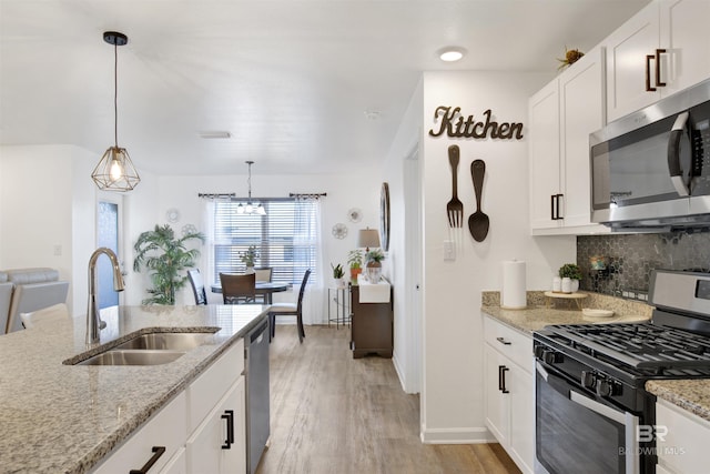 kitchen featuring light stone counters, stainless steel appliances, sink, white cabinetry, and hanging light fixtures