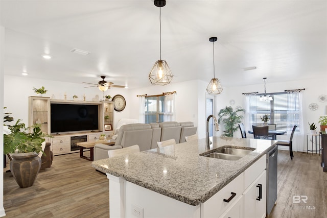 kitchen featuring light stone counters, sink, white cabinets, hanging light fixtures, and an island with sink