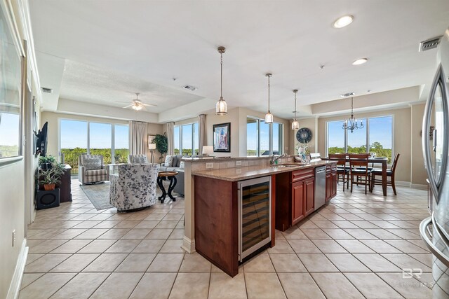 kitchen featuring hanging light fixtures, appliances with stainless steel finishes, a tray ceiling, beverage cooler, and light stone countertops