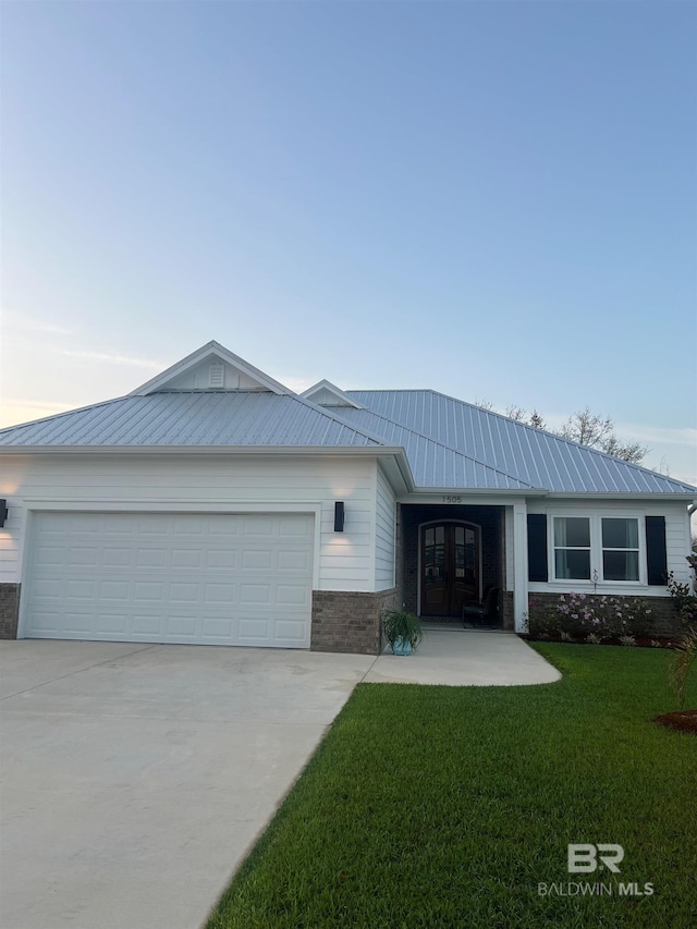 ranch-style home with concrete driveway, metal roof, french doors, an attached garage, and a front lawn