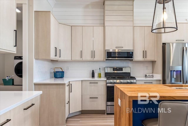 kitchen with decorative backsplash, light wood-type flooring, washer / dryer, and appliances with stainless steel finishes