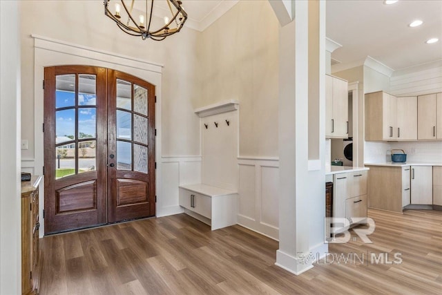 foyer with crown molding, french doors, a wainscoted wall, arched walkways, and light wood finished floors