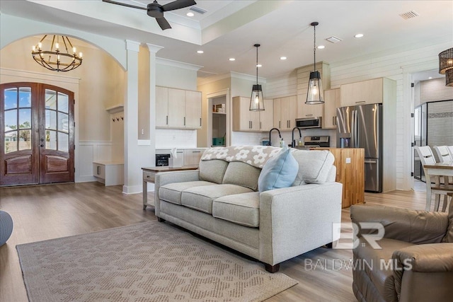 living room featuring arched walkways, visible vents, ceiling fan with notable chandelier, and light wood finished floors