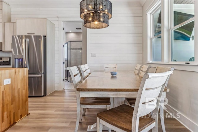 dining area featuring an inviting chandelier, wood walls, and light wood-type flooring