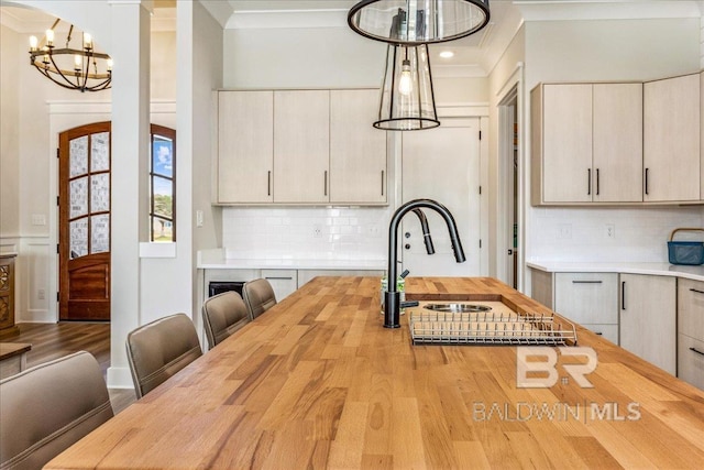 kitchen with a notable chandelier, a sink, butcher block counters, and crown molding