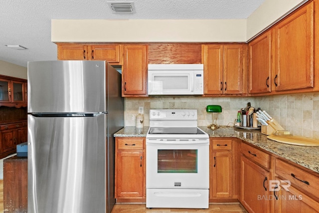 kitchen with decorative backsplash, a textured ceiling, white appliances, and light stone counters