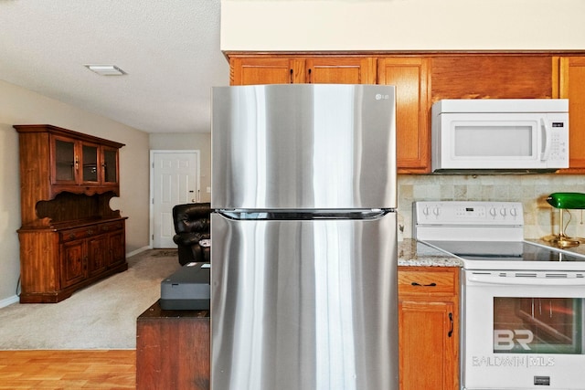 kitchen with a textured ceiling, white appliances, light colored carpet, and backsplash