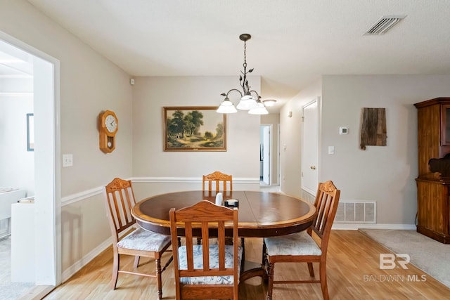 dining space with light hardwood / wood-style flooring and an inviting chandelier