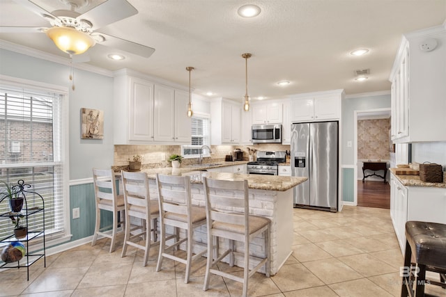 kitchen featuring kitchen peninsula, appliances with stainless steel finishes, crown molding, white cabinetry, and hanging light fixtures