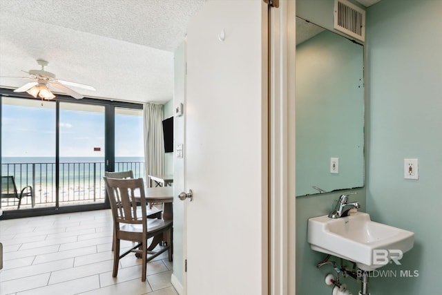 interior space with ceiling fan, sink, expansive windows, a textured ceiling, and a water view