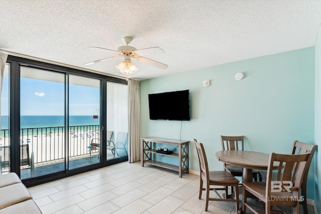 interior space featuring a view of the beach, a textured ceiling, a wall of windows, and ceiling fan