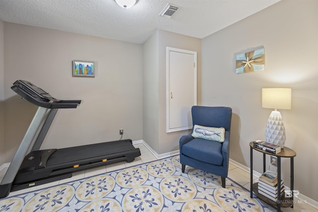 workout area with a textured ceiling, baseboards, visible vents, and tile patterned floors