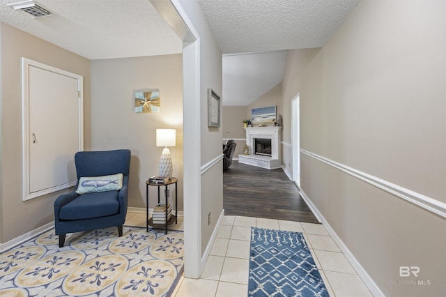 hall with light tile patterned floors, baseboards, visible vents, and a textured ceiling