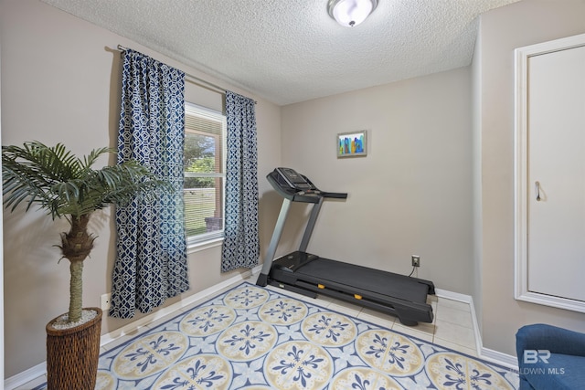 exercise room featuring baseboards, tile patterned floors, and a textured ceiling