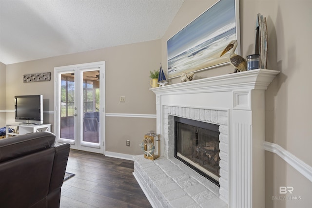 living area featuring lofted ceiling, a textured ceiling, a brick fireplace, wood-type flooring, and baseboards
