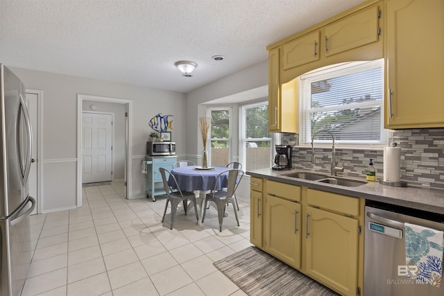 kitchen with light tile patterned floors, a sink, a textured ceiling, appliances with stainless steel finishes, and decorative backsplash