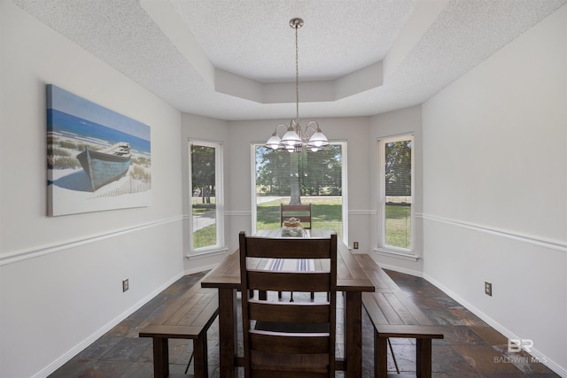 dining space featuring a tray ceiling, a notable chandelier, stone tile flooring, a textured ceiling, and baseboards