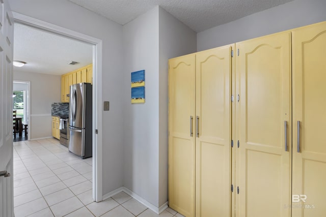 hall featuring a textured ceiling, baseboards, and light tile patterned floors