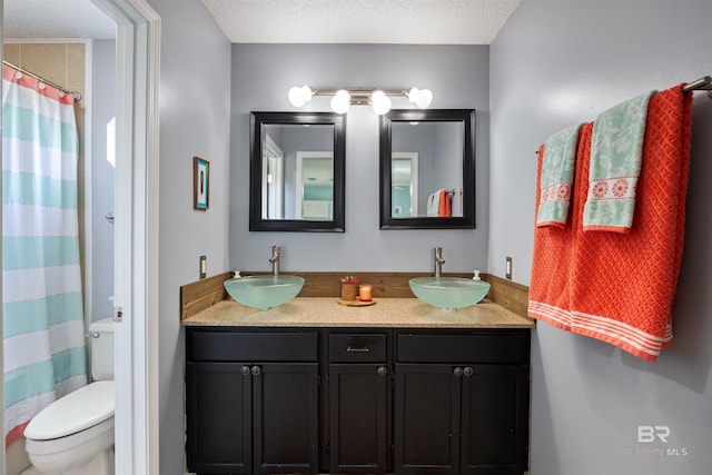 bathroom featuring a textured ceiling, toilet, double vanity, and a sink