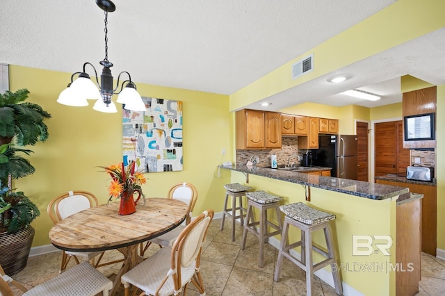 kitchen with backsplash, hanging light fixtures, light tile patterned floors, kitchen peninsula, and stainless steel refrigerator