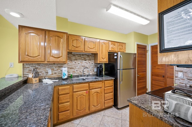 kitchen featuring sink, a textured ceiling, tasteful backsplash, light tile patterned flooring, and stainless steel refrigerator