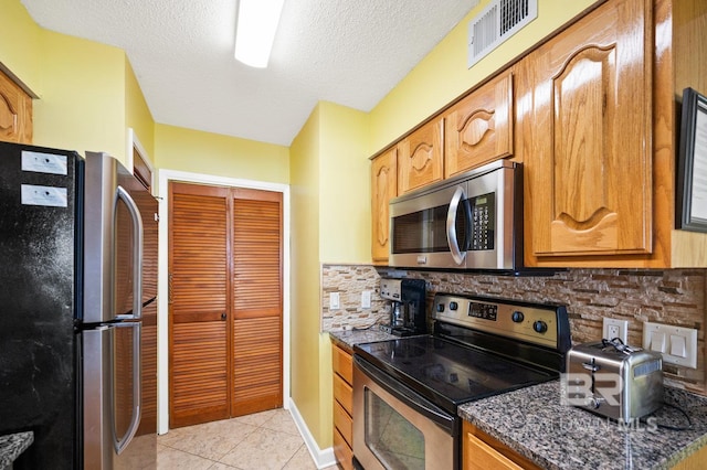 kitchen featuring dark stone counters, decorative backsplash, light tile patterned floors, and stainless steel appliances