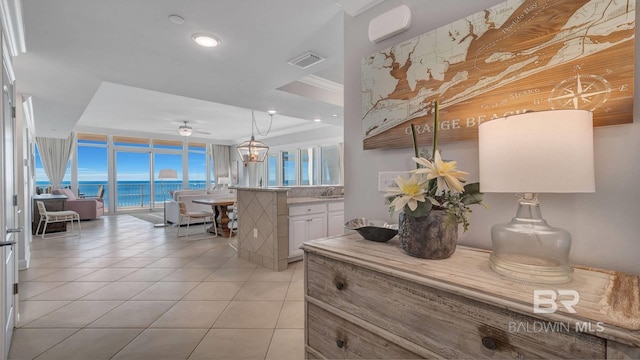 kitchen with decorative light fixtures, a water view, white cabinetry, sink, and light tile floors