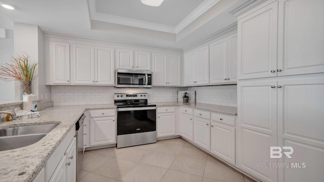 kitchen featuring stainless steel appliances, a tray ceiling, backsplash, and white cabinetry